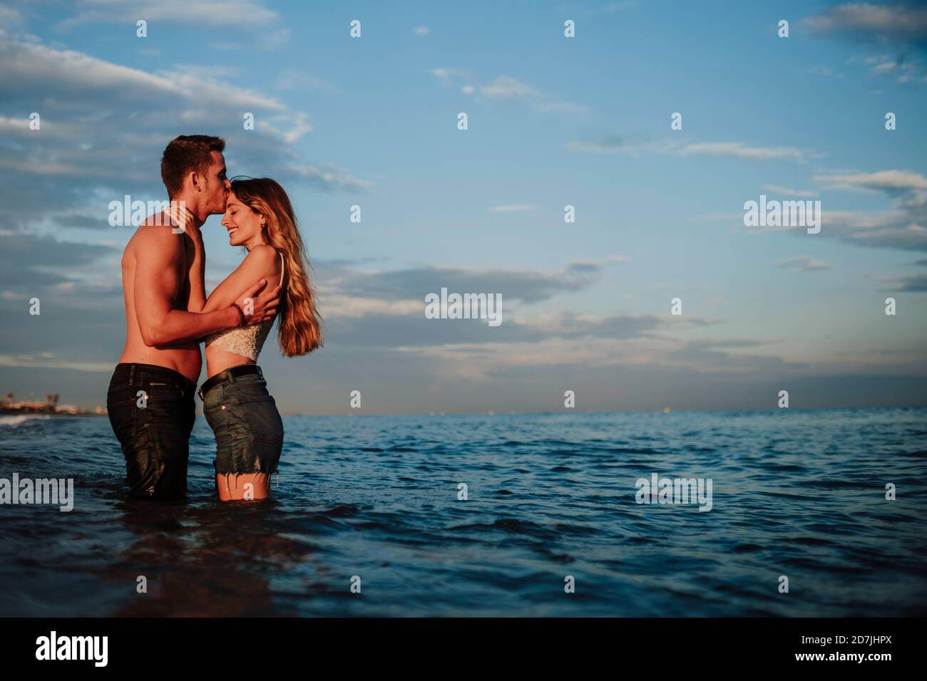 Boyfriend kissing girlfriend while standing in water at beach Stock Photo