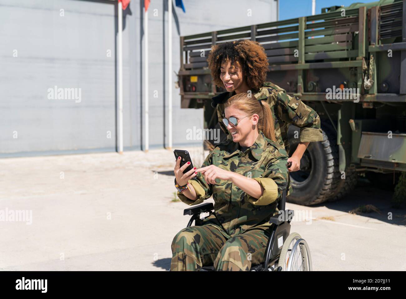 Smiling disabled female soldier taking selfie with young colleague against truck at army base on sunny day Stock Photo