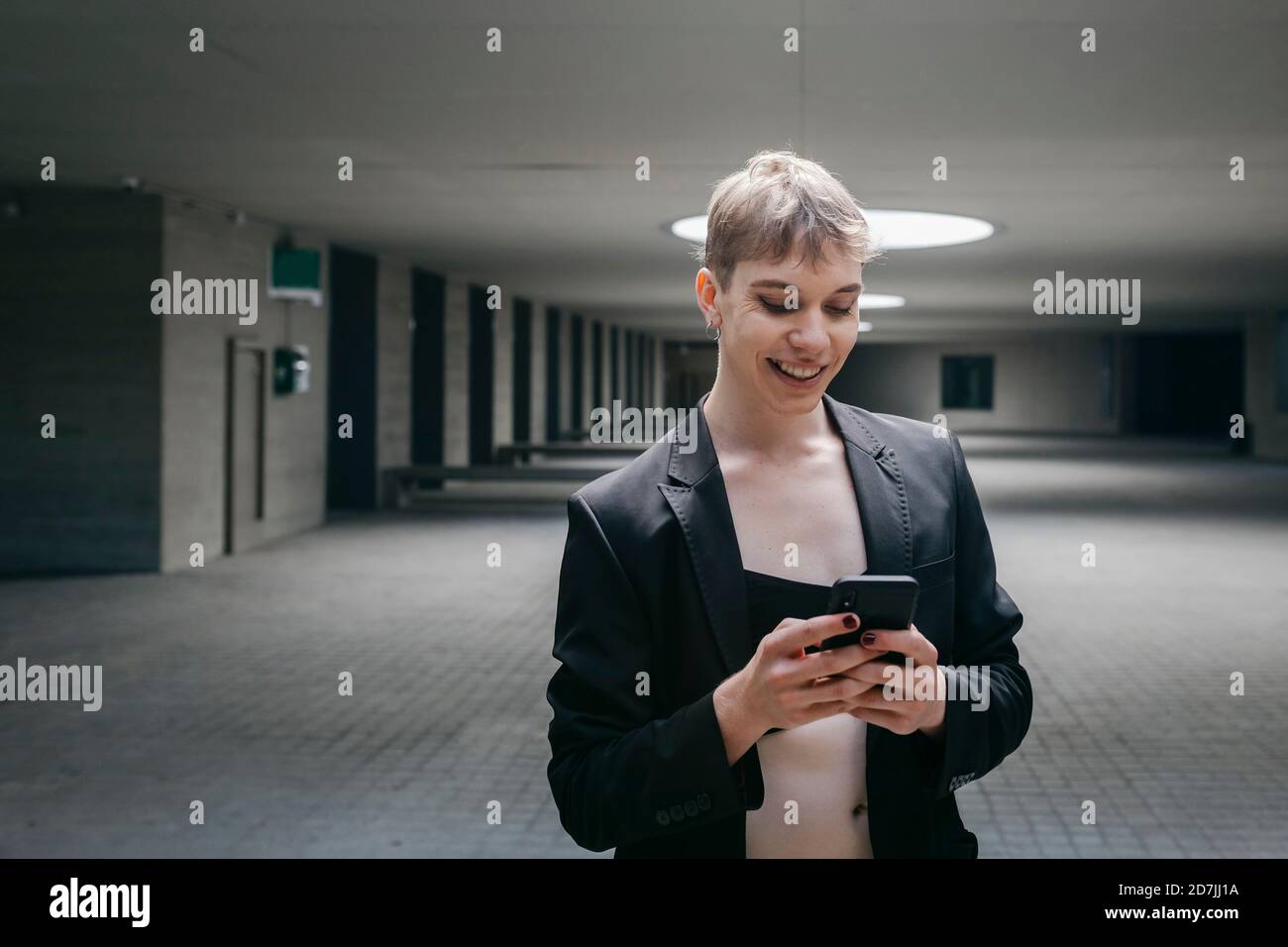 Smiling trans young man using mobile phone while standing in basement Stock Photo