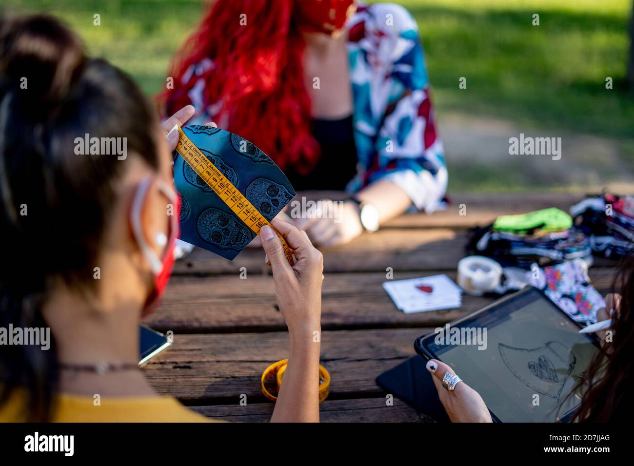 Friends measuring and designing face mask while sitting outdoors Stock Photo
