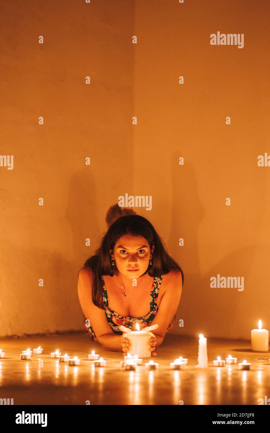 Mid adult woman lying by lit candles against wall in darkroom at home Stock Photo