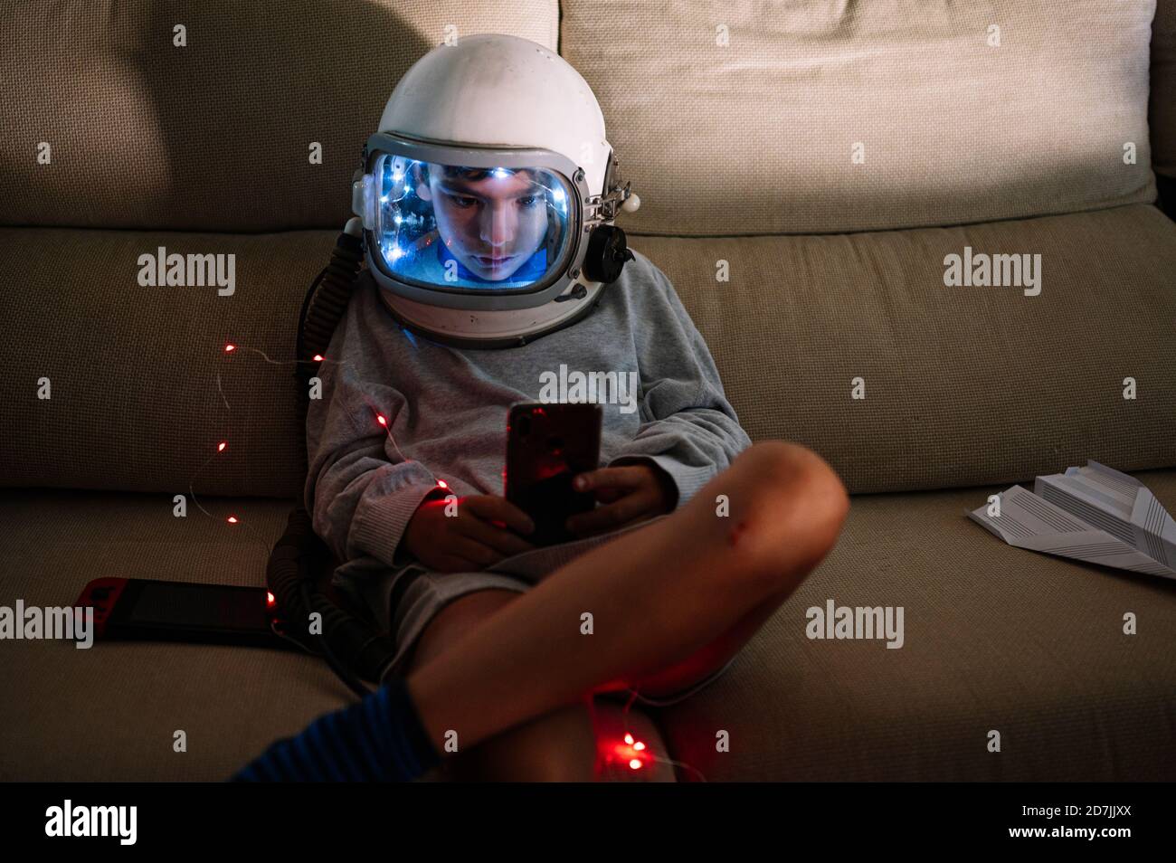 Boy wearing space helmet using smart phone while sitting with ...