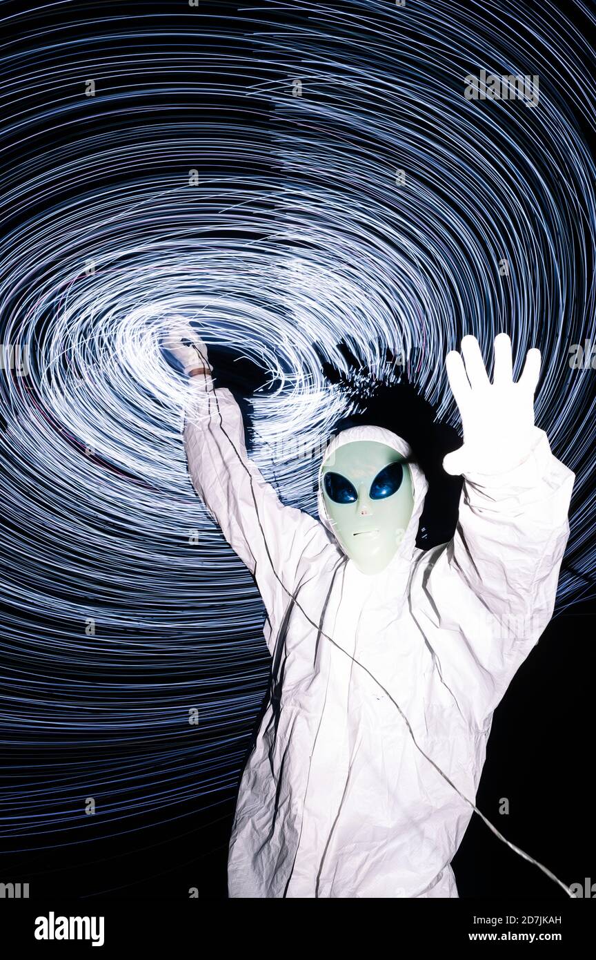 Man in white alien costume standing under light trails at night Stock Photo