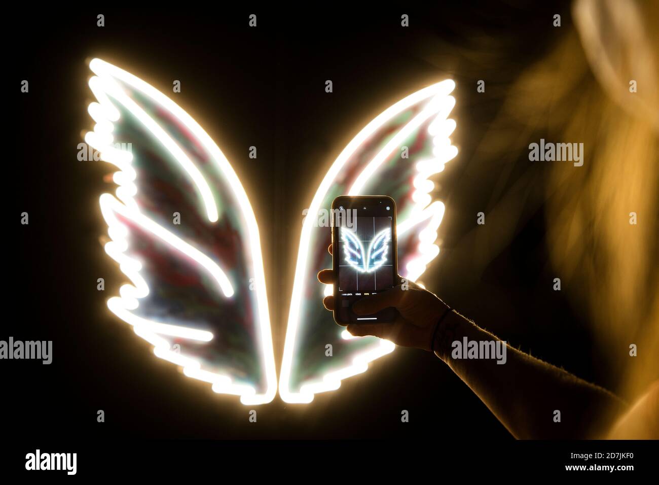 Arm of young woman taking smart phone photo of white glowing neon wings Stock Photo