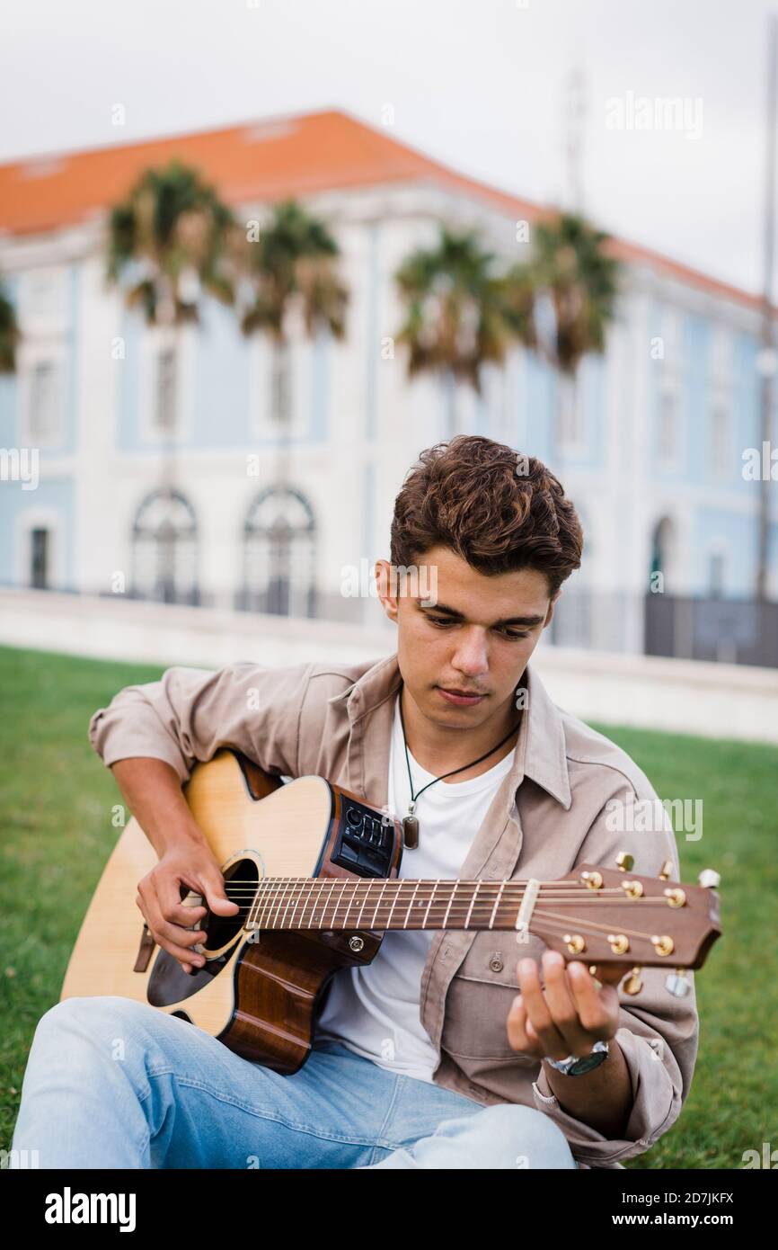 Handsome young man practicing guitar while sitting on grass at park Stock Photo