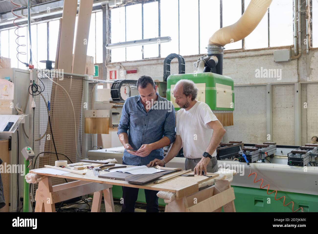 Project manager and coworker working while standing against sawing machine at factory Stock Photo