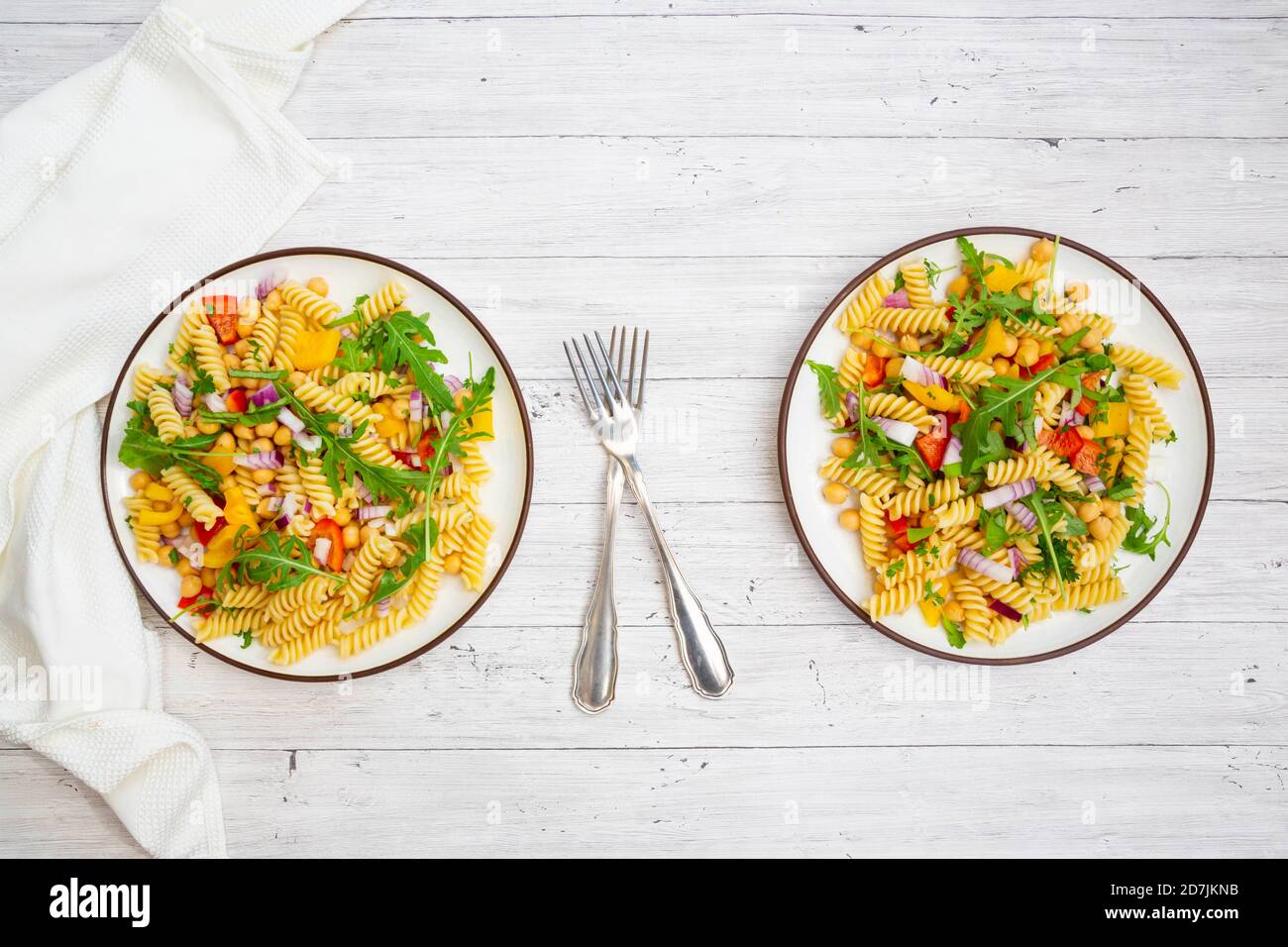 Two plates of vegetarian pasta salad with chick-peas, bell pepper, arugula, onion, parsley and basil Stock Photo