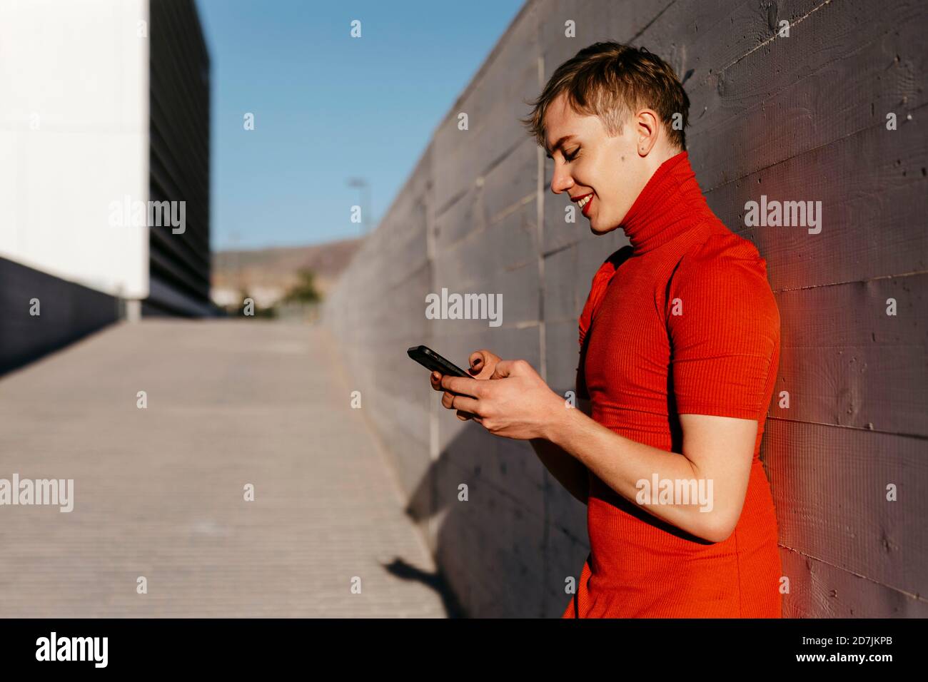 Non-binary man text messaging on smart phone while standing against wall Stock Photo