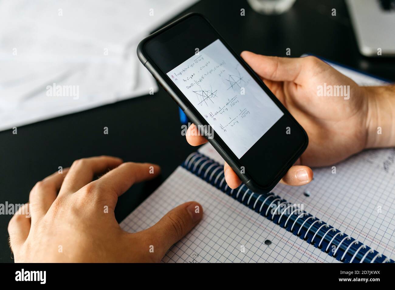 Hands of male adult student holding smart phone with mathematical equation at home Stock Photo