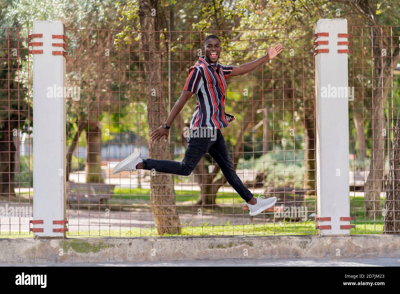Cheerful young man jumping against fence at park Stock Photo