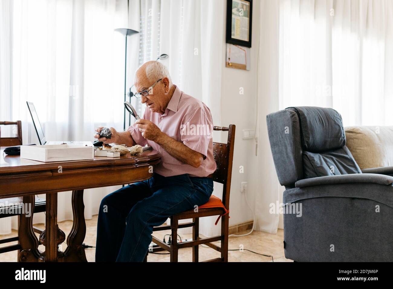 Retired elderly man using magnifying glass for research of fossil and mineral at home Stock Photo