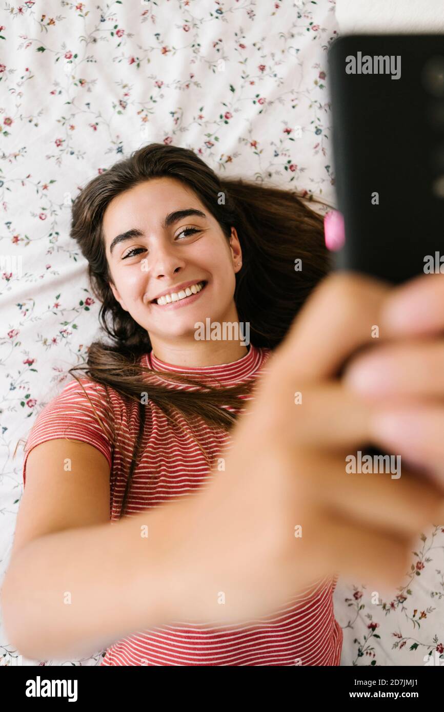 Smiling woman taking selfie on smart phone in bedroom Stock Photo