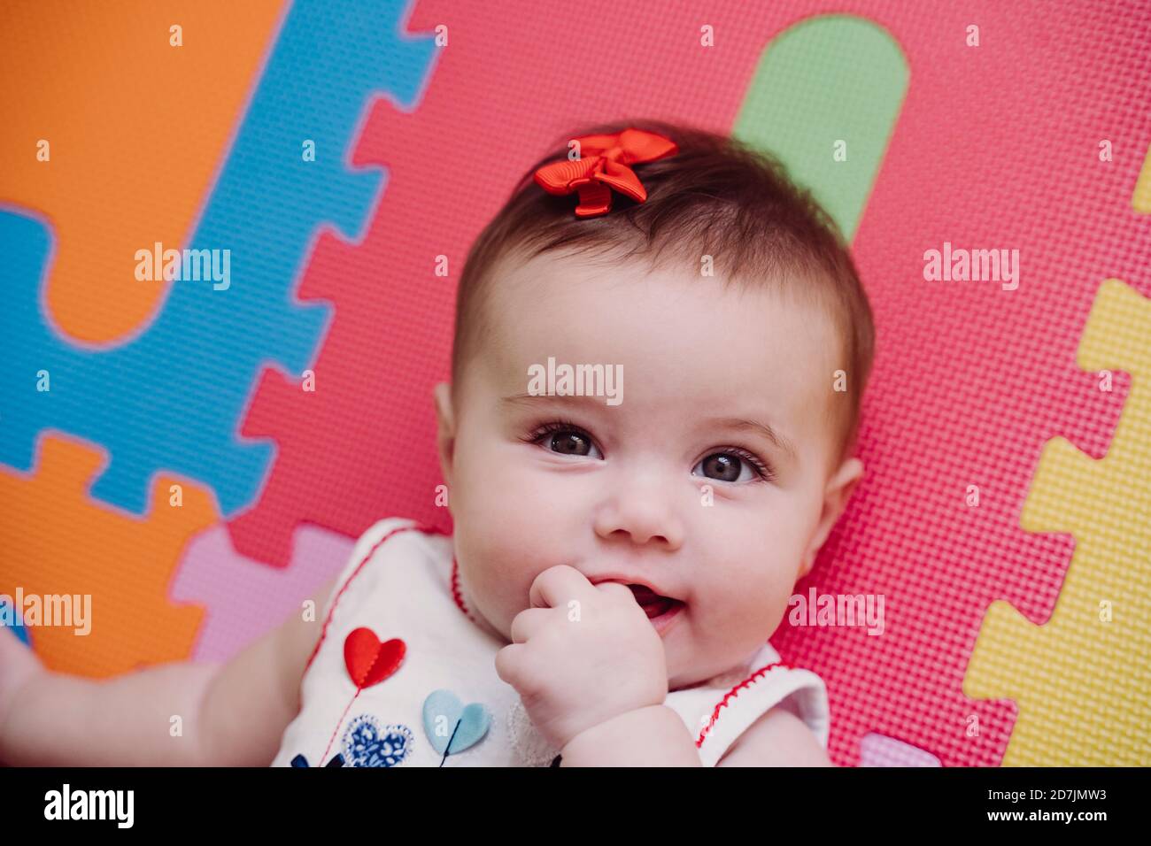 Close Up Portrait Of Cute Baby Girl With Finger In Mouth Lying On Puzzle Playmat At Home Stock Photo Alamy