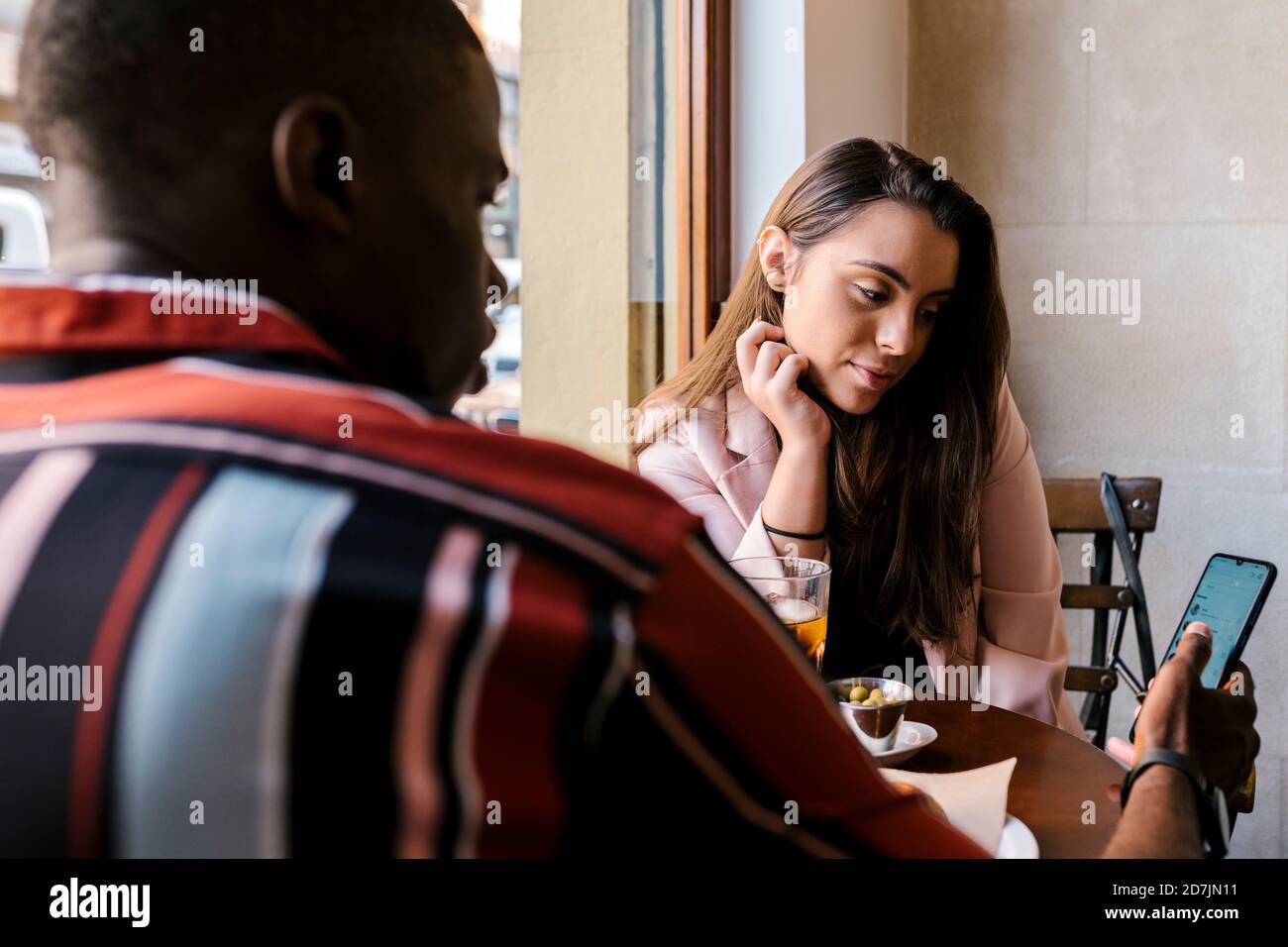 Young man showing mobile phone to girlfriend while sitting in cafe Stock Photo