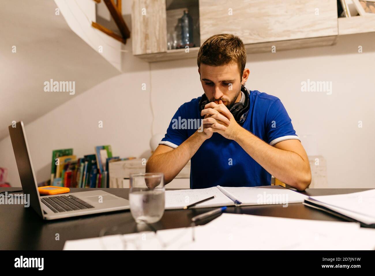 Dedicated young male student sitting with hands clasped while doing homework at table Stock Photo