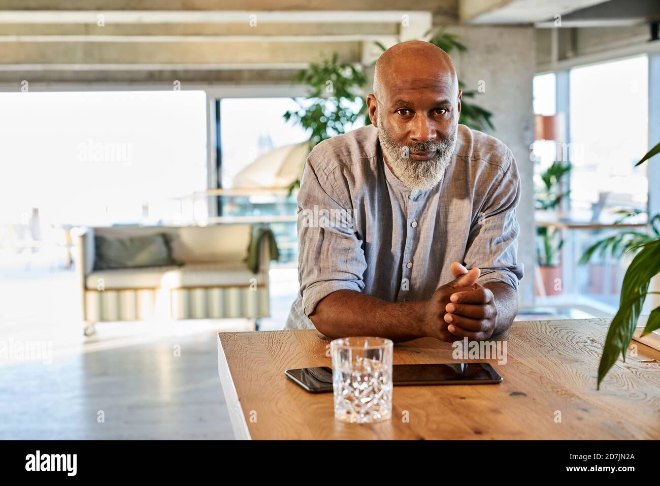Confident bald man with hands clasped leaning on table at rooftop Stock Photo