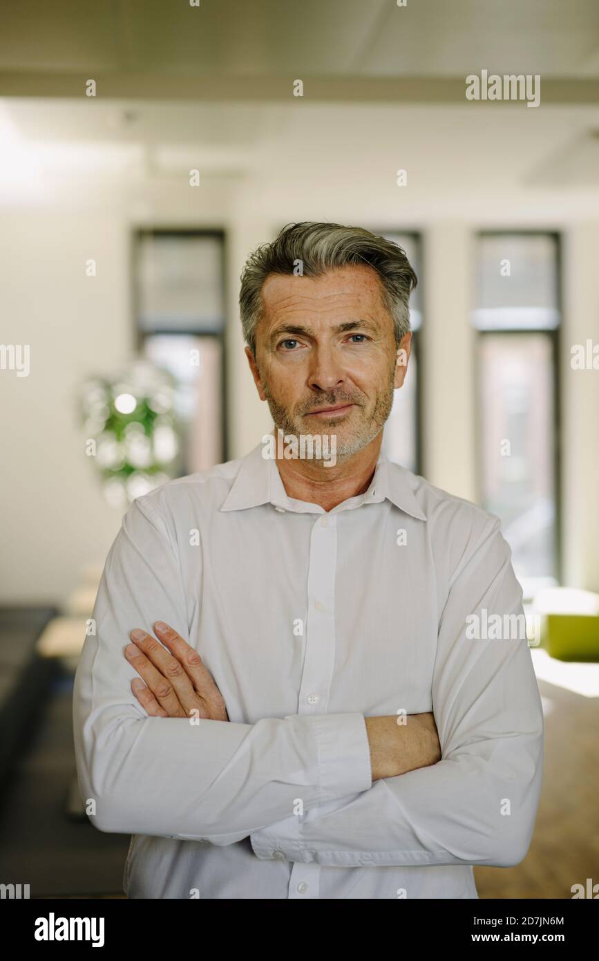Confident businessman with arms crossed standing at office Stock Photo ...