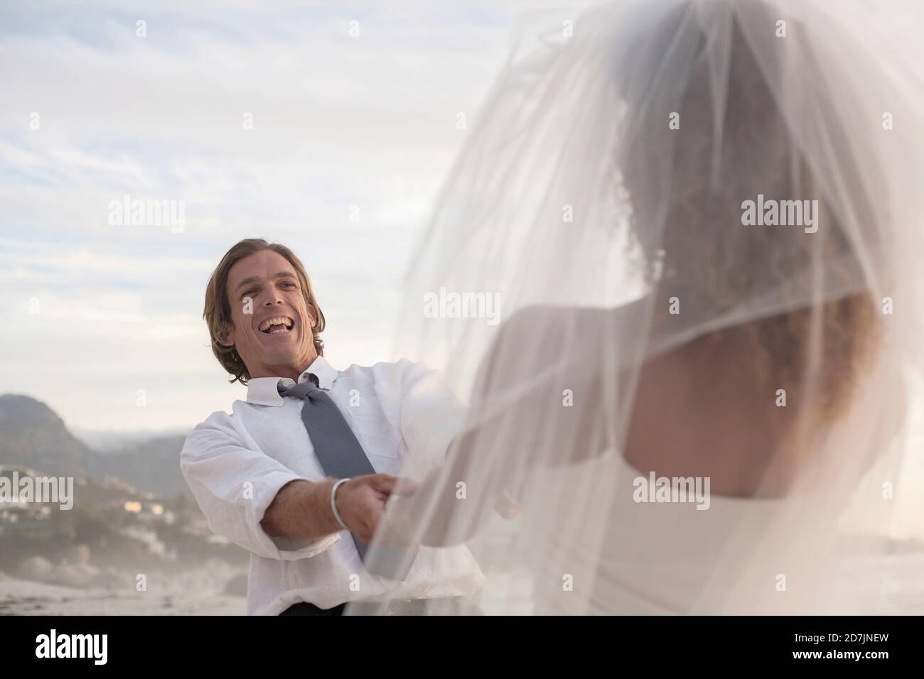 Carefree bridegroom holding hands of bride against sky at sunset Stock Photo