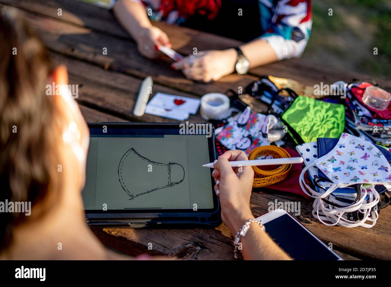 Friends designing face mask on digital tablet while sitting outdoors Stock Photo