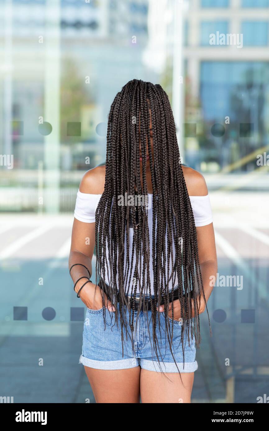 Young woman covering face with hair while standing against glass wall in city Stock Photo