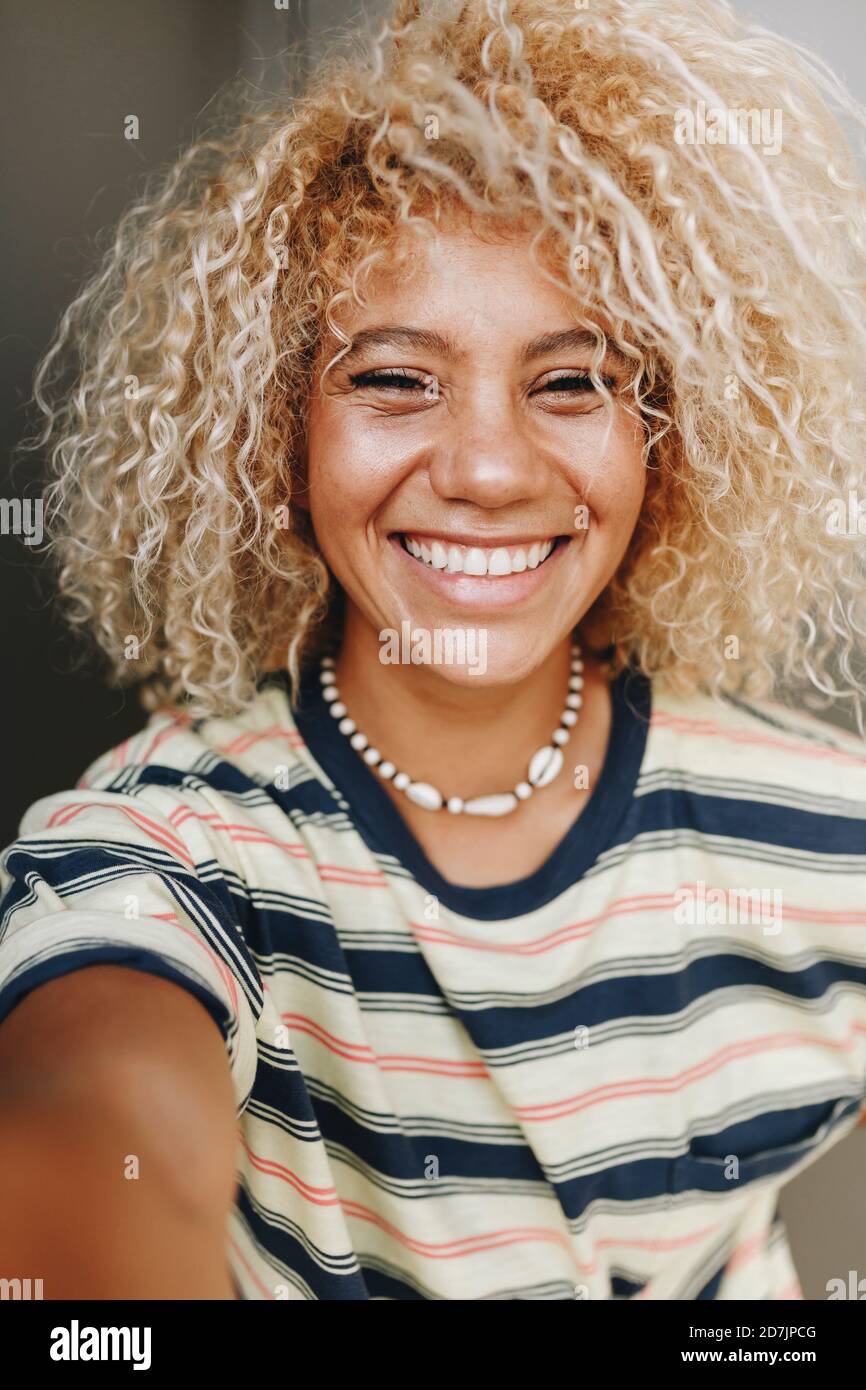 Happy Hispanic woman with blond curly hair taking selfie Stock Photo