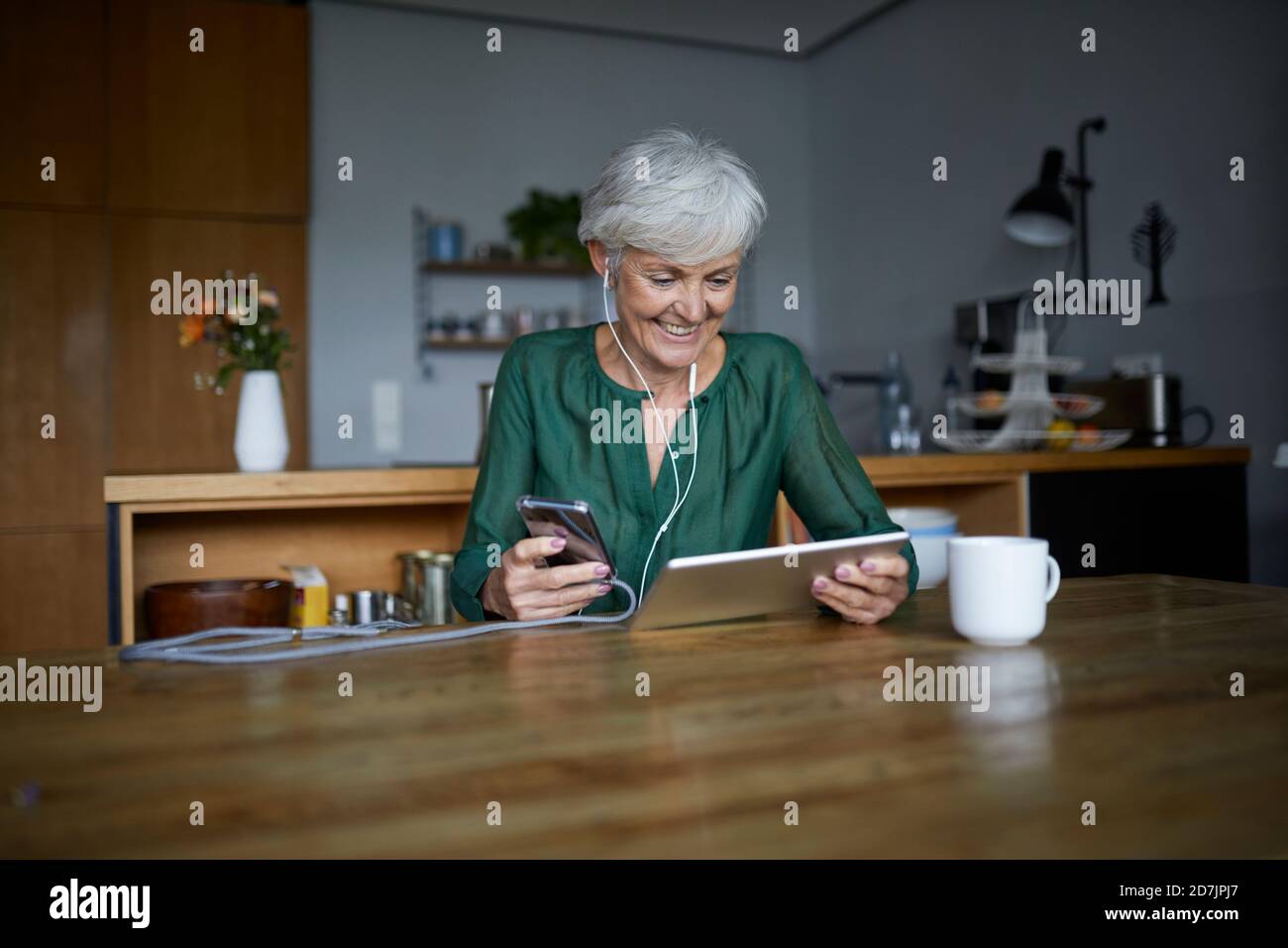 Senior woman listening to music while using smart phone and digital tablet at home Stock Photo
