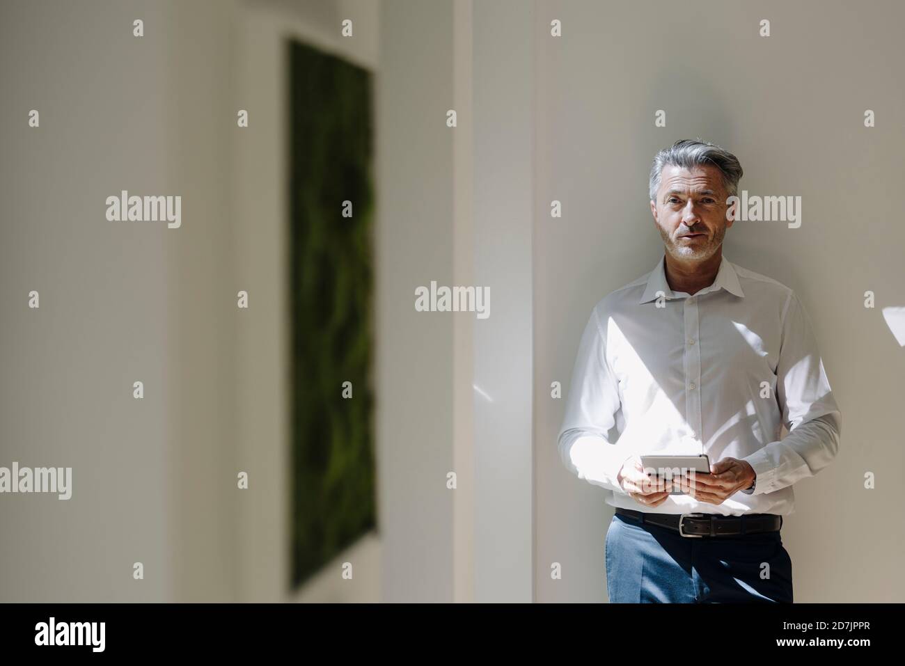 Man using digital tablet while leaning on wall at office Stock Photo