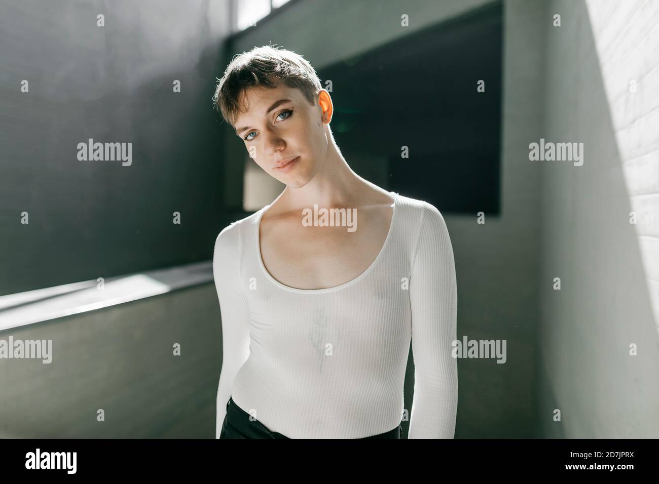 Trans young man wearing white leotard standing in basement Stock Photo