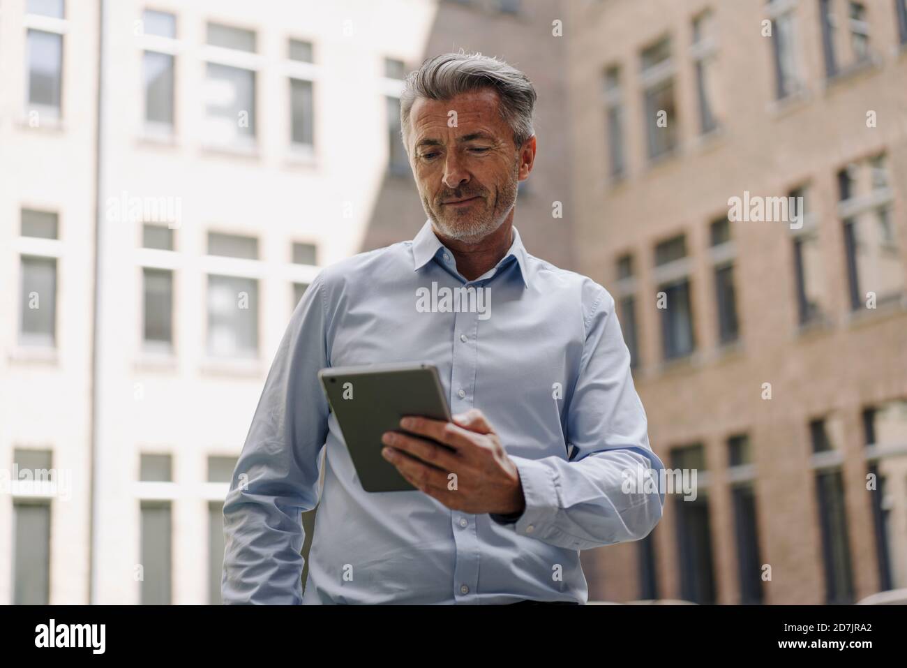 Businessman using digital tablet while standing against building Stock Photo