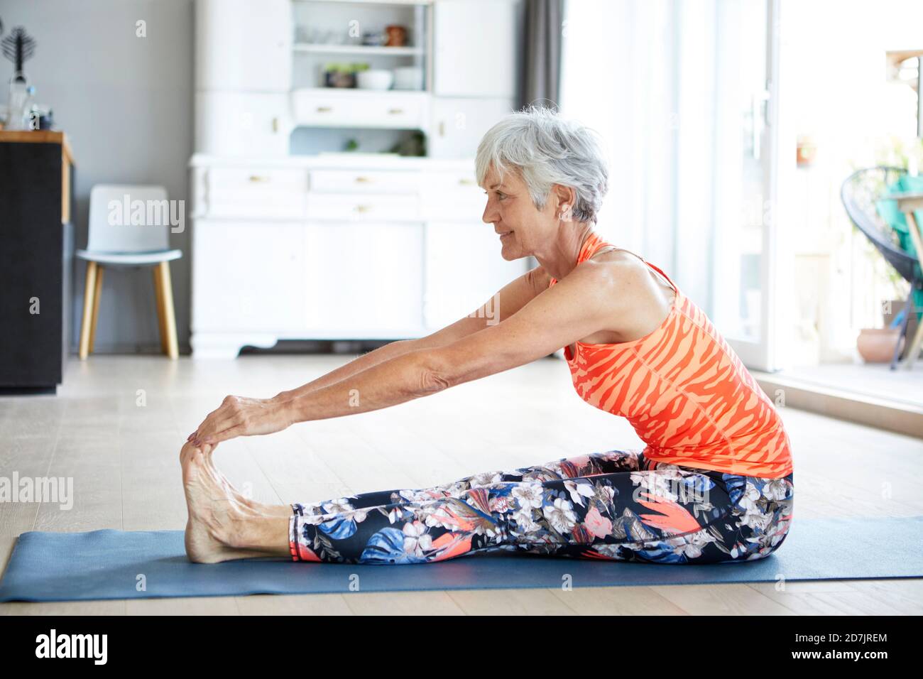 Fit senior woman stretching leg and back while exercising at home Stock Photo