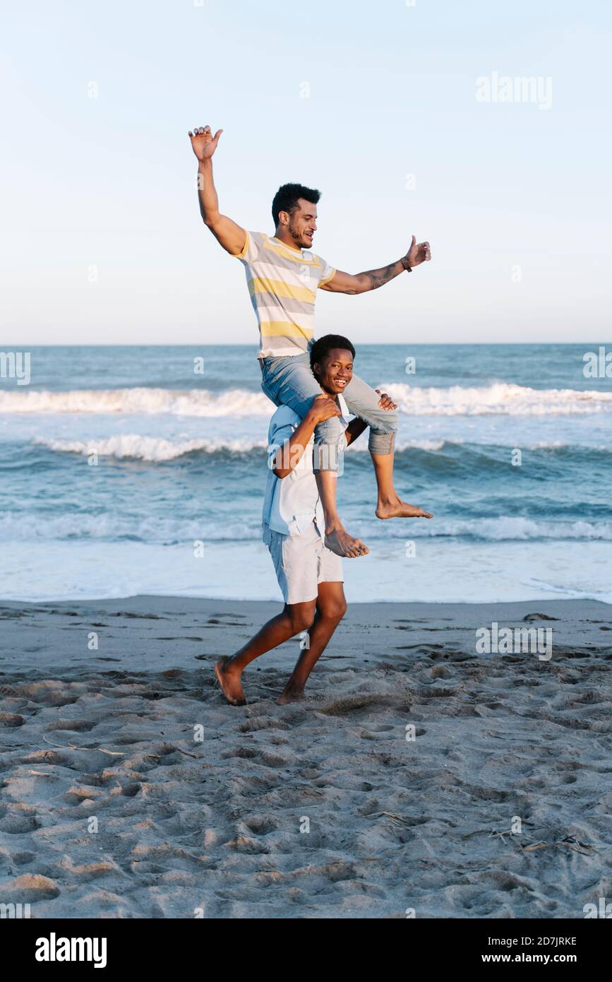 Young man carrying friend on shoulder at beach Stock Photo