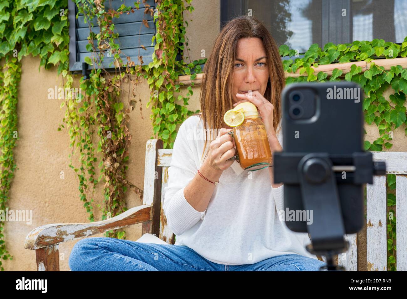 Female nutritionist drinking juice from jar while vlogging through smart phone at back yard Stock Photo