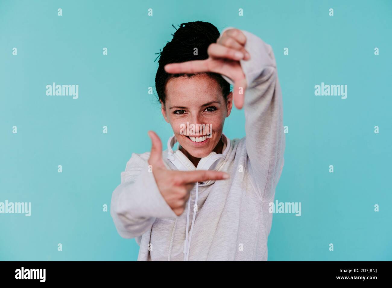 Smiling beautiful woman making frame with fingers against turquoise background Stock Photo