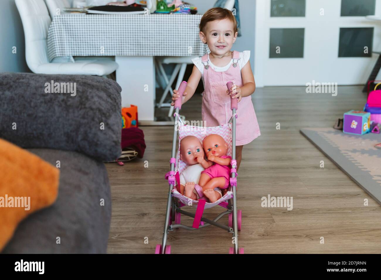 Baby girl playing with baby stroller and doll at home Stock Photo