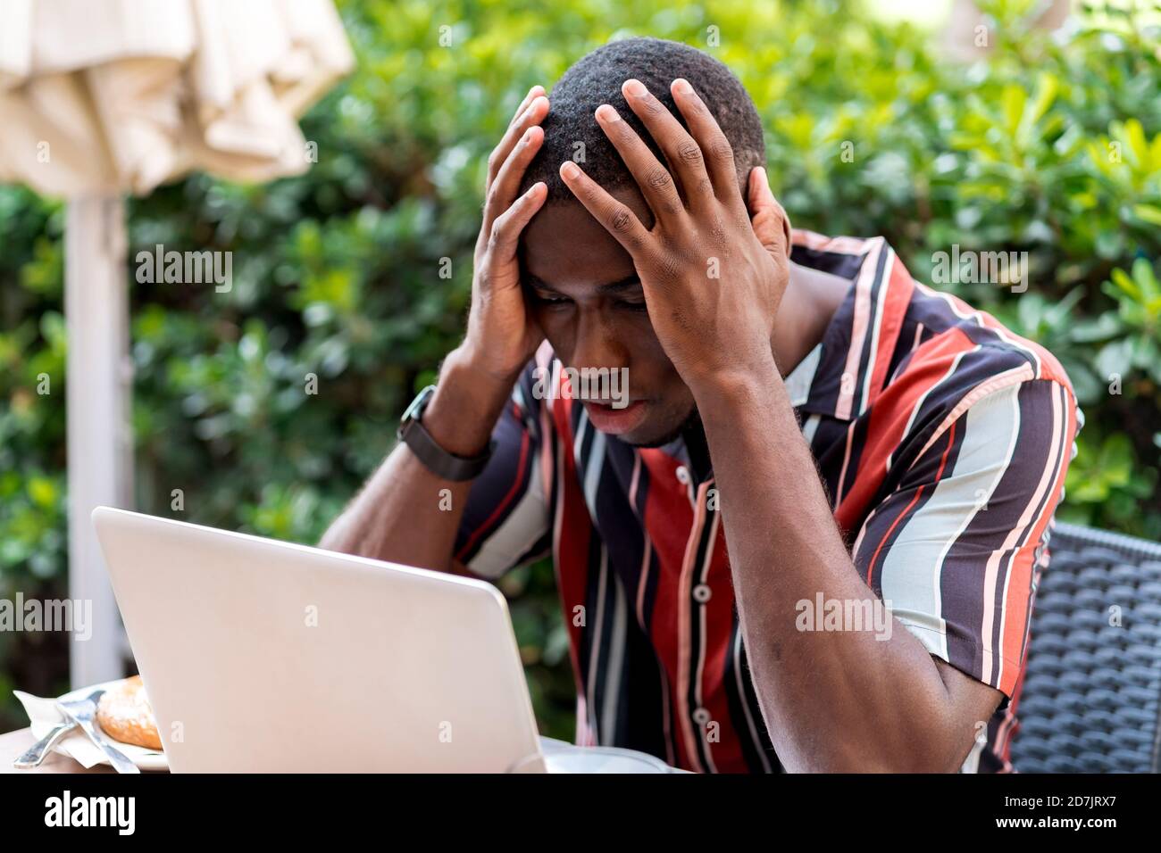 Tensed young man sitting with head in hands while looking at laptop in cafe Stock Photo