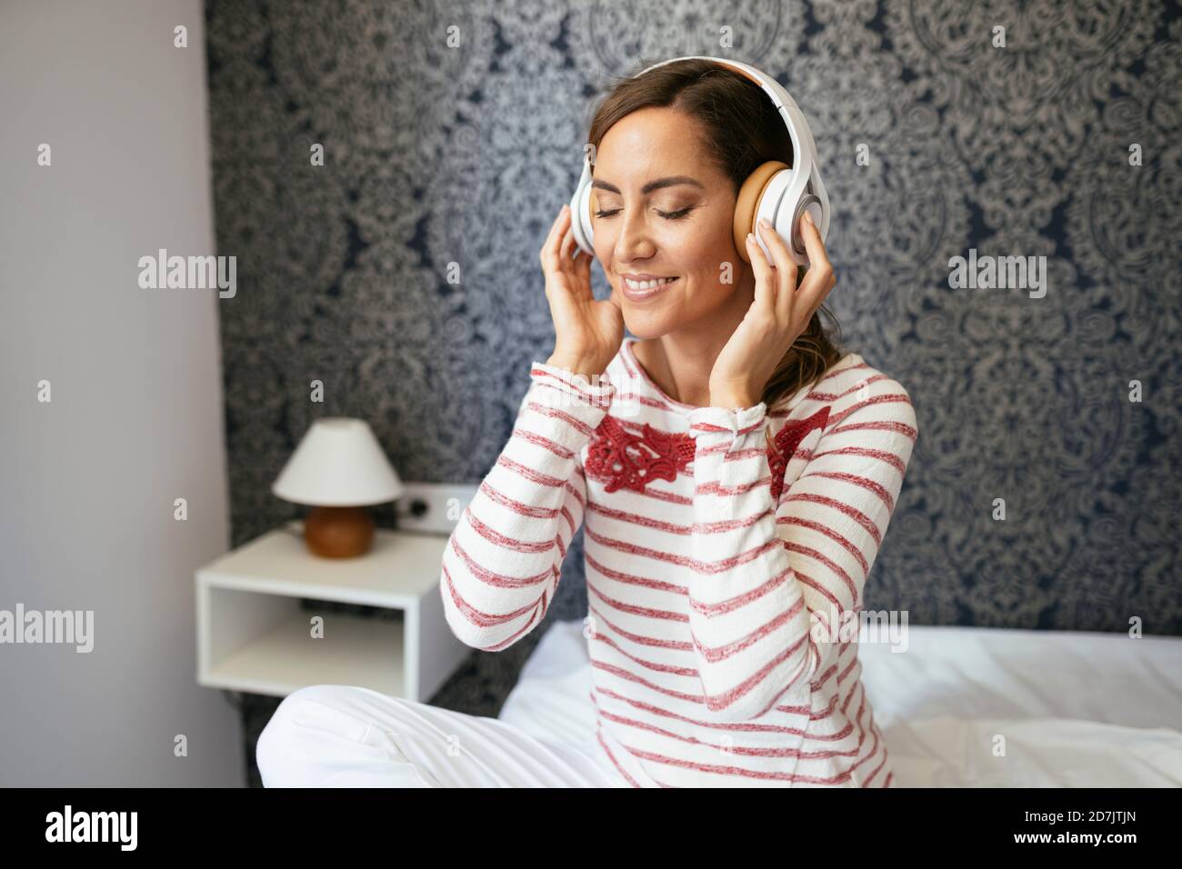 Smiling woman with eyes closed listening music while sitting on bed at home Stock Photo