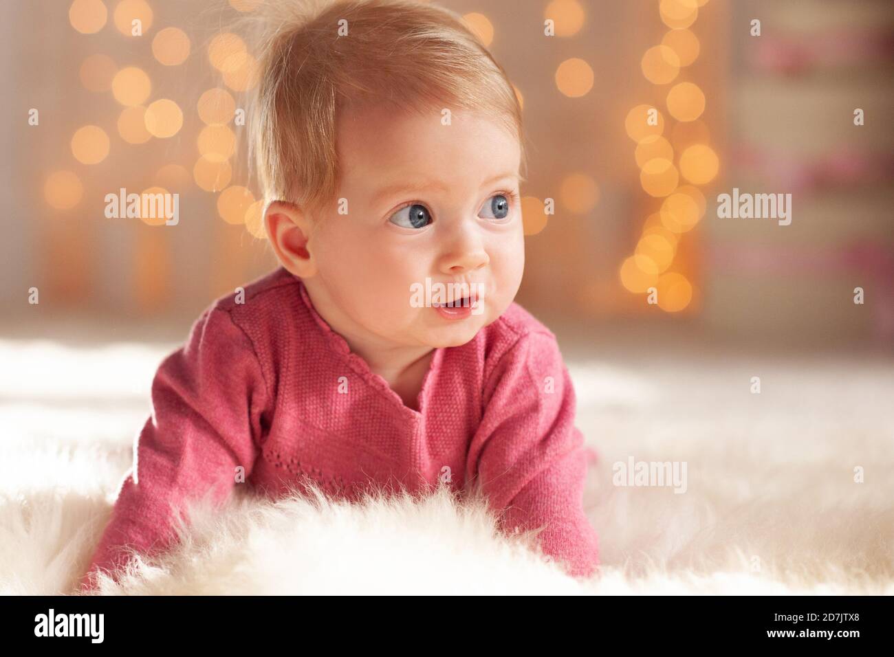 Pretty baby girl under 1 year old wearing knitted pink sweater over Christmas glowing lights in room close up. Winter holiday season. Childhood. New Y Stock Photo Alamy