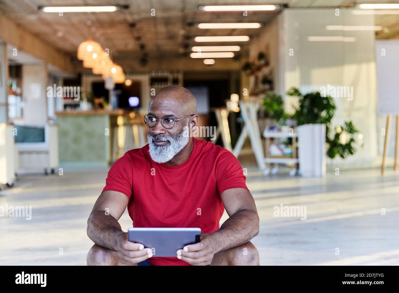 Thoughtful man holding digital tablet and looking away while sitting at rooftop Stock Photo