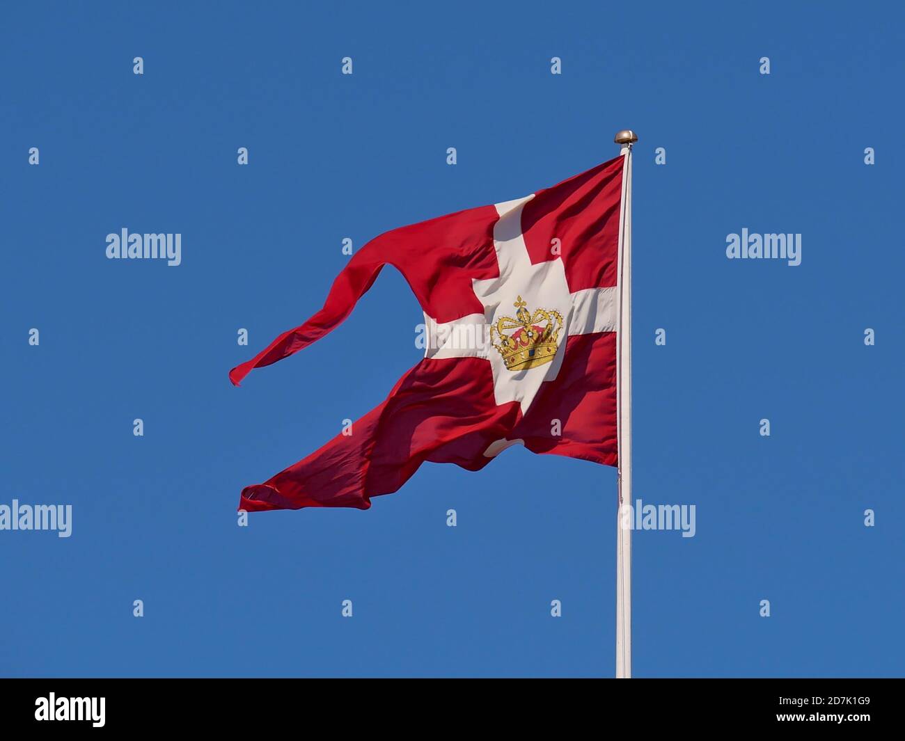 The royal standard flag (red ground with white cross and a golden crown in center) of the Danish royal family flying in the wind above Amalienborg . Stock Photo