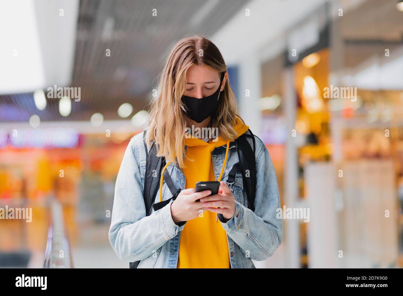 Woman in protective mask with cell phone at a shopping centre or underground. Living in pandemic world, urban scene Stock Photo