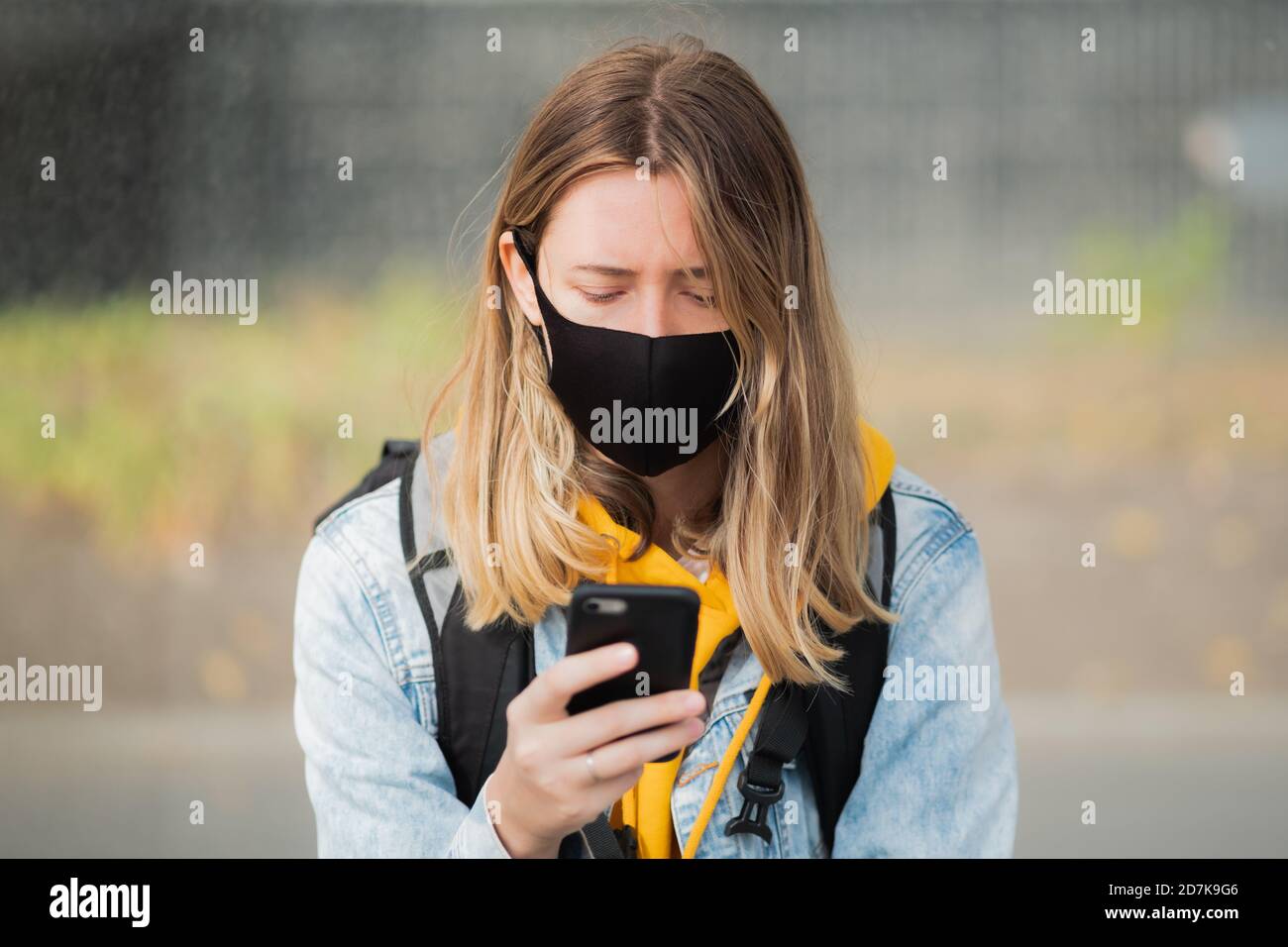 Woman in mask with a cell phone. Young female using smartphone at public place, covid time Stock Photo