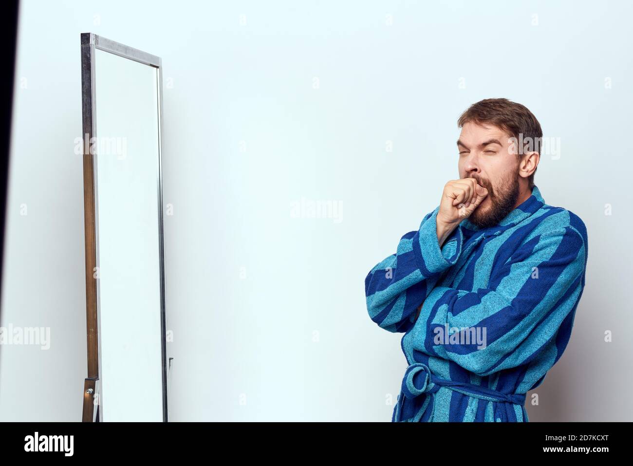 a man in a blue robe examines himself in a mirror in a bright room ...