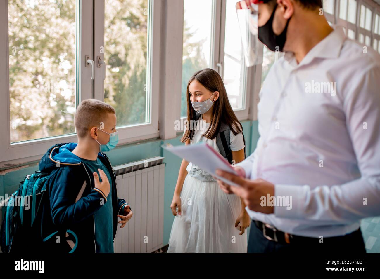 Elementary school students and male teacher wearing protective face ...