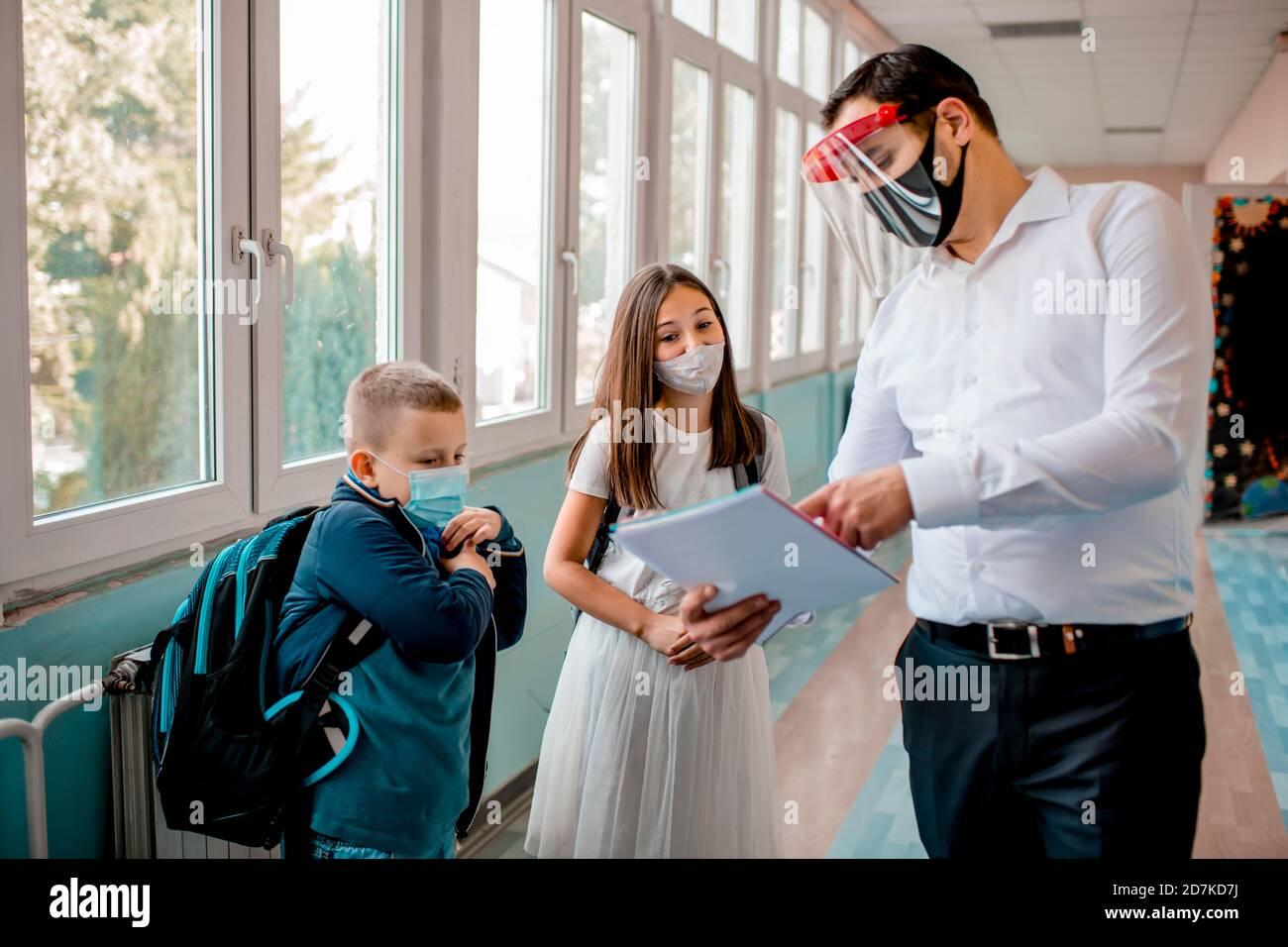 Elementary school students and male teacher wearing protective face ...