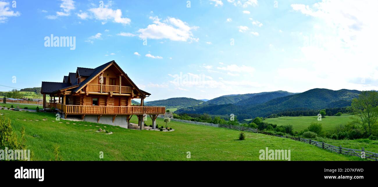 Mountain timbered cottage on green meadow. Wooden building with a romantic view. Stock Photo