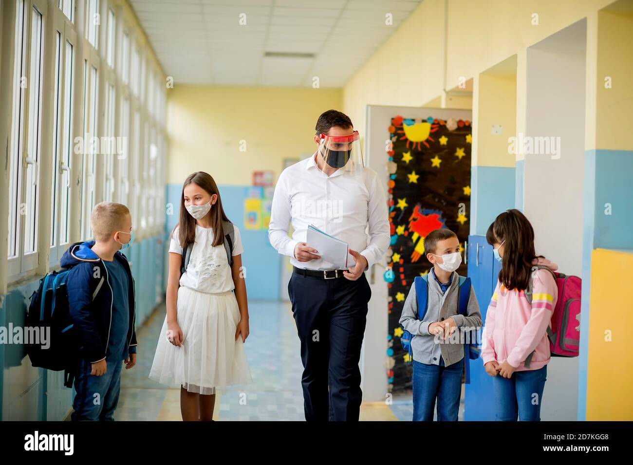 Elementary school students and male teacher wearing protective face ...
