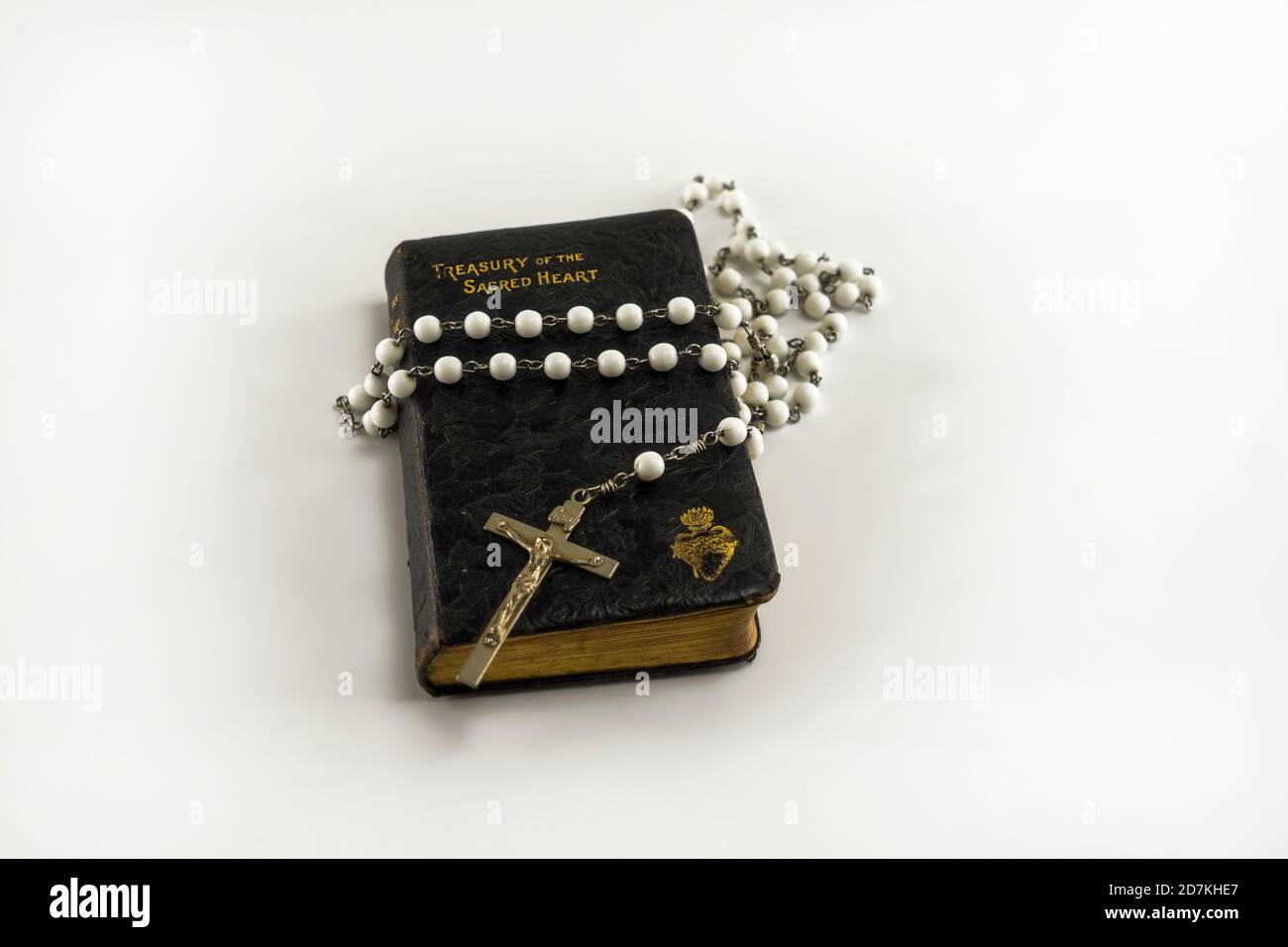 Closed old brown leather catholic holy prayer book Treasury of the Sacred Heart and white beads crucifix with holy cross isolated on a white backgroun Stock Photo