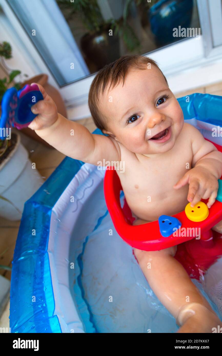Baby taking a bath and playing in a little inflatable pool. Toddler having fun indoor his home