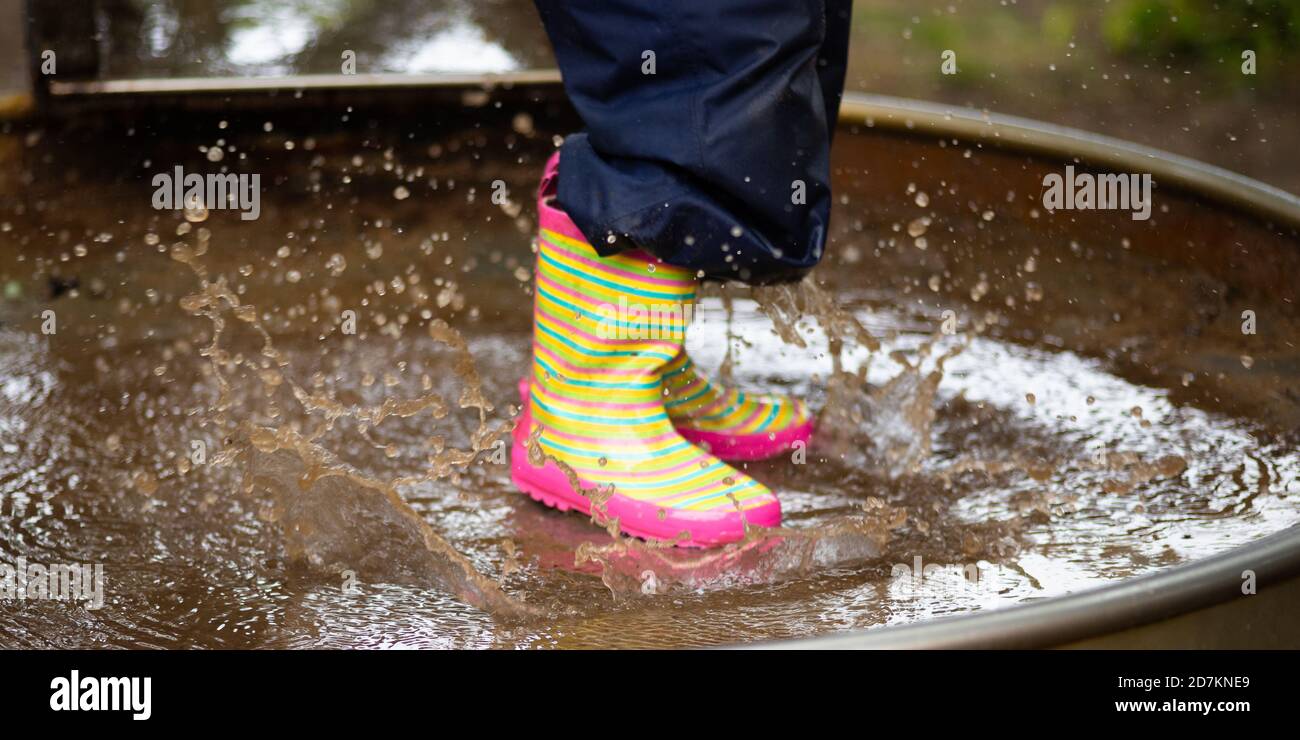 Detail of colorful rubber boots of a child jumping into a puddle of mud ...