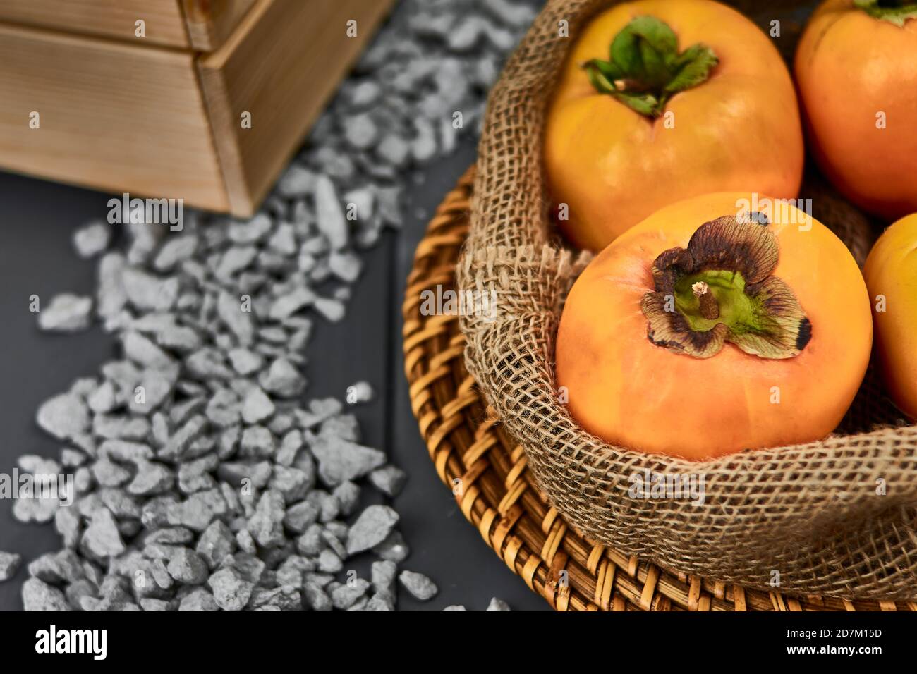 Sack of delicious persimmons. Autumn fruit. kakis. wooden box. stones. gray and orange tones Stock Photo